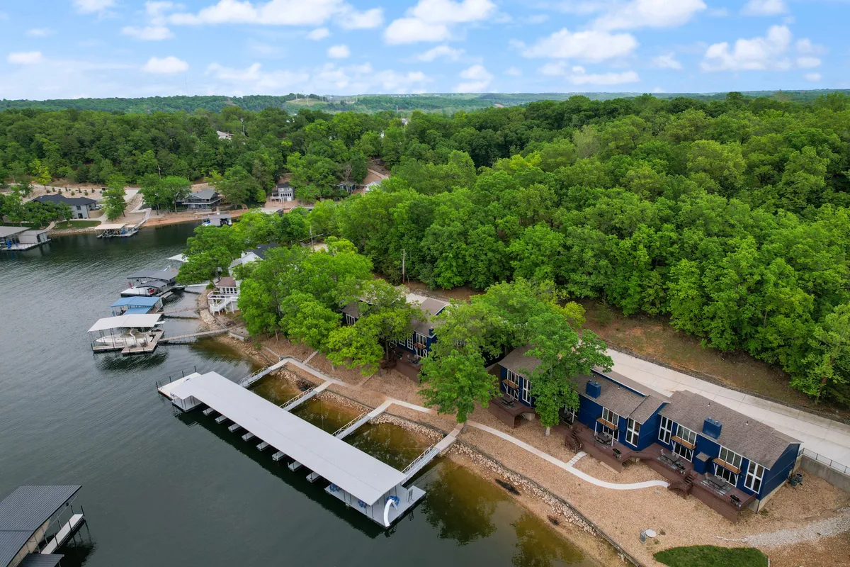 A broad lakeside view featuring multiple docks, clear blue water, lush greenery along the shore, and an expansive sky. This perspective emphasizes a playful, inviting waterfront—perfect for swimming, sunbathing, and group activities.