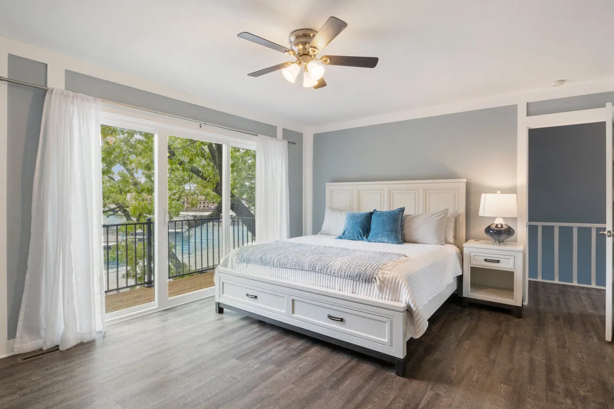 A serene bedroom featuring a bed with soft, neutral bedding, a nightstand with a gentle-glow lamp, and a large window letting in natural light. The window offers a calming view of the outdoors, enhancing the tranquil ambiance. The space feels uncluttered and welcoming, perfect for relaxation and recharging.