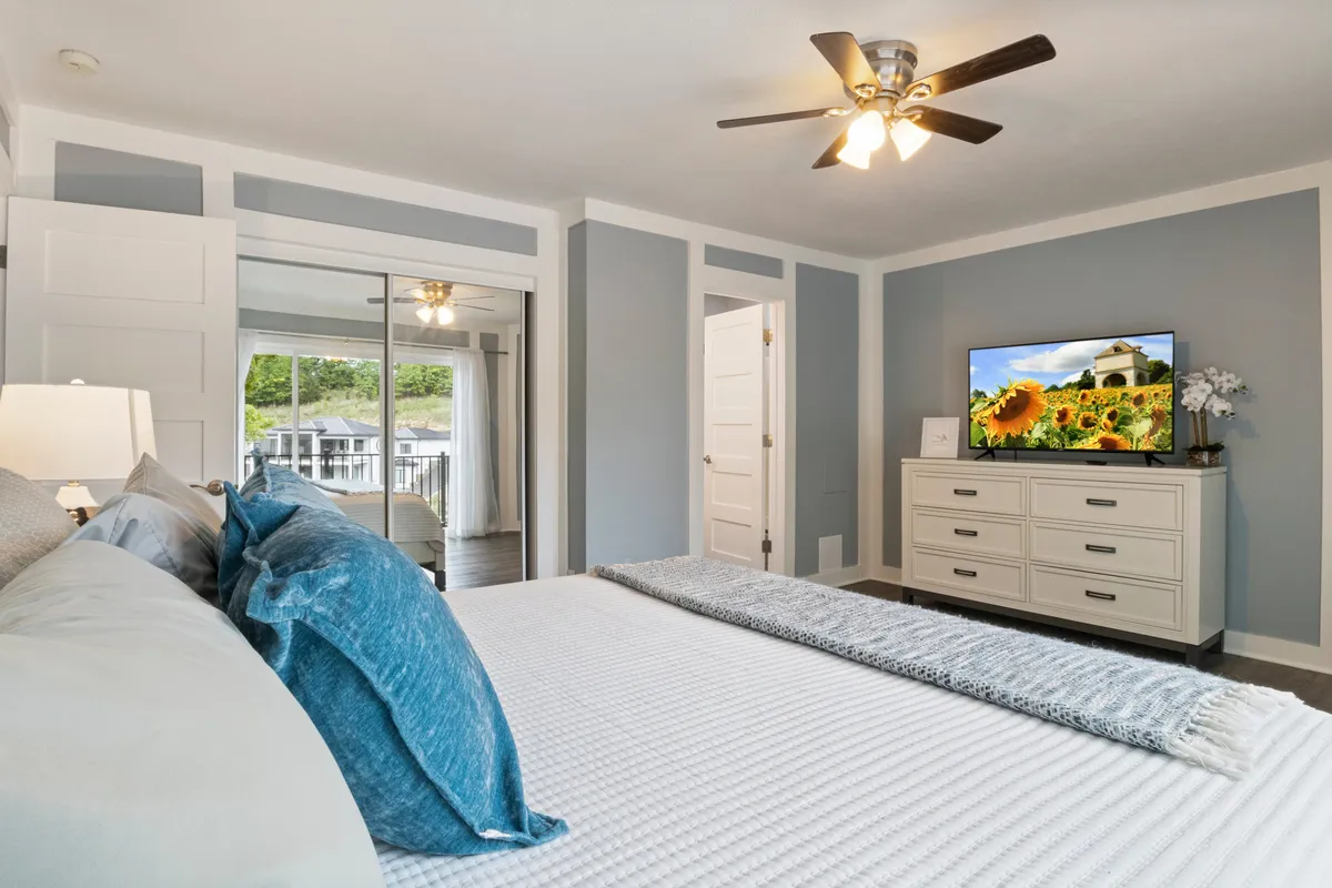 A spacious and comfortable bedroom with a decorative pillow-adorned bed, a television displaying a scenic image, a well-styled dresser, and soft ambient lighting. The decor is understated and soothing, making the space feel both practical and peaceful for guests of all ages and needs.
