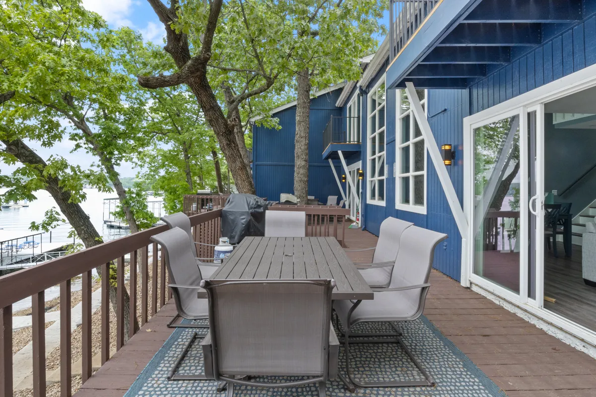 An outdoor dining table is set on a deck or dock area with lush green trees framing a panoramic waterfront view. The scene is ideal for alfresco gatherings, offering a space for snacks, drinks, and relaxed conversation just steps from the water.