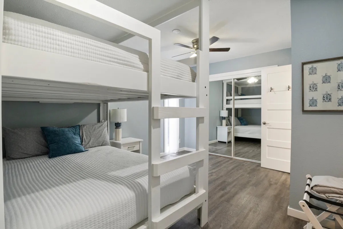 A family-friendly bedroom featuring both a double bed and a bunk bed, complete with colorful decorative pillows and a dresser with a mirror. The room is well-lit, spacious, and designed for shared moments, making it suitable for families or groups, plus there’s ample floor space for pet beds or crates.