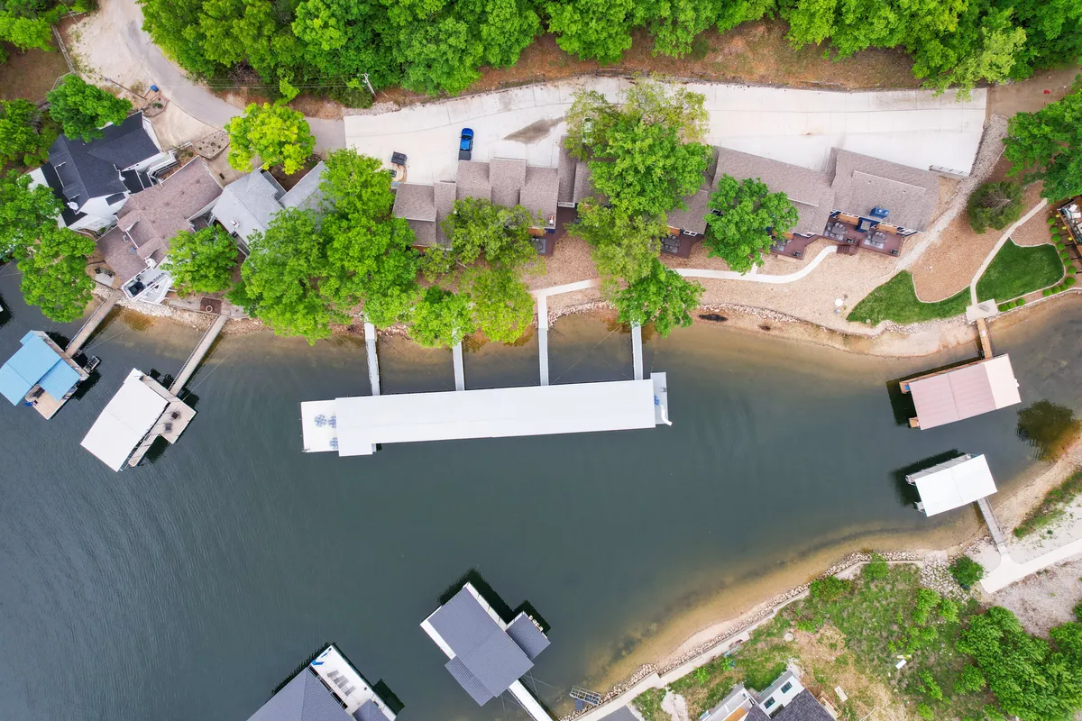 This image presents a serene view of the private dock stretching over calm waters, surrounded by lush trees and neighboring houses. The tranquil waterway hints at opportunities for swimming, boating, and relaxing by the lake, while the openness of the dock suggests space for sunbathing and socializing.