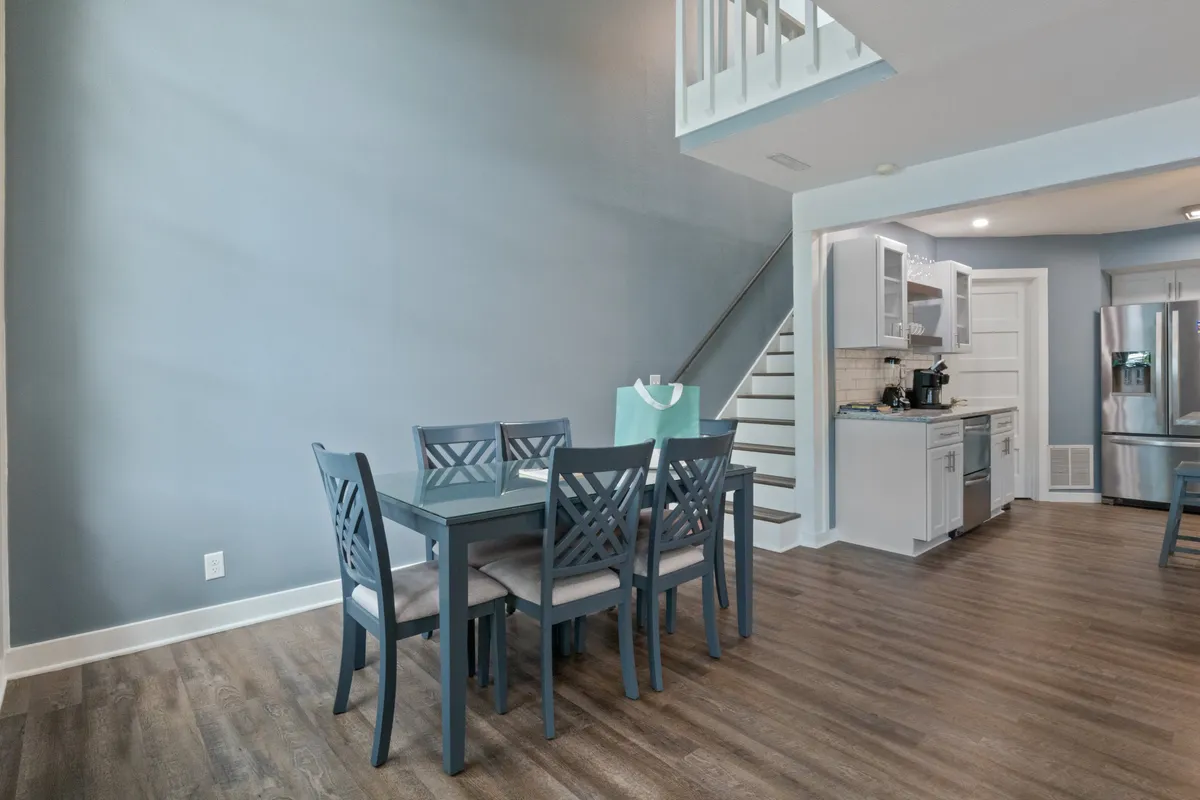 A welcoming dining area with a family-sized table, kitchen appliances in the background, and a staircase leading to other parts of the home. The scene suggests a lively, adaptable space for family meals or casual gatherings.